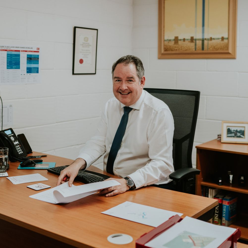 A man sat behind a desk smiling at a computer monitor